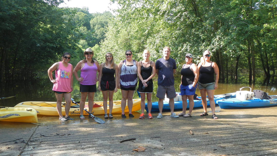 seven women and one man pose for a picture with the kayaks behind them