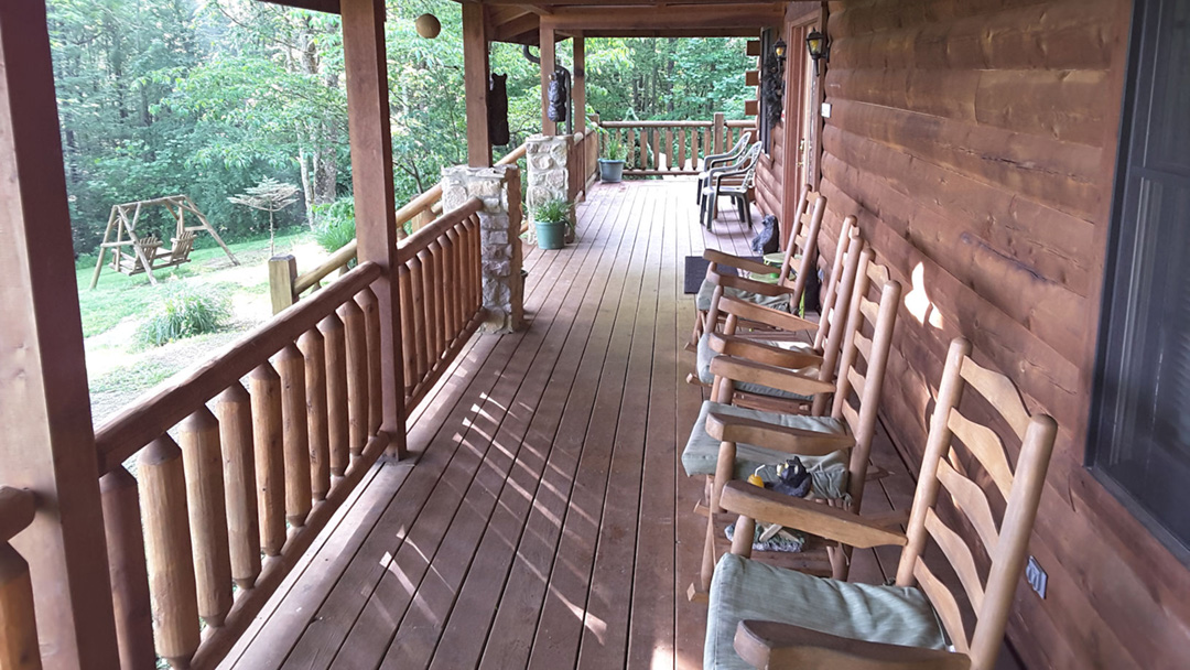 View of a long wooden porch with rocking chairs at Adveturewood Log Cabin