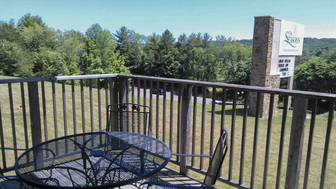 Image from a balcony with a rod iron patio setting in the foreground, "The Seasons" sign and lush woods in the background