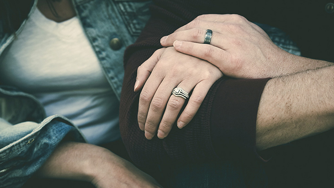 Hands of a man and woman are wrapped around the man's arm