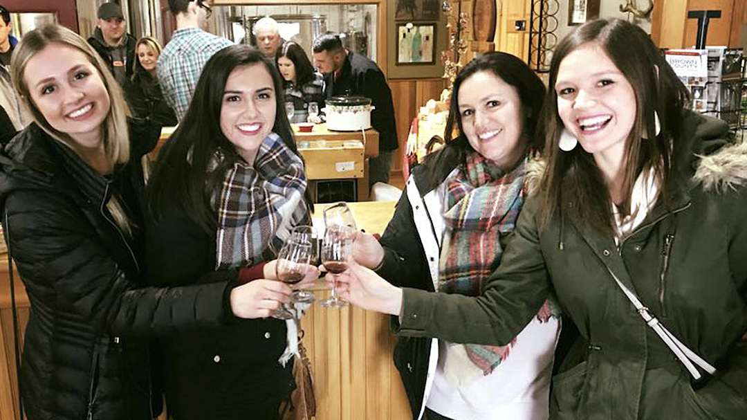 Four young ladies toast with a glass of wine as they smile for the camera