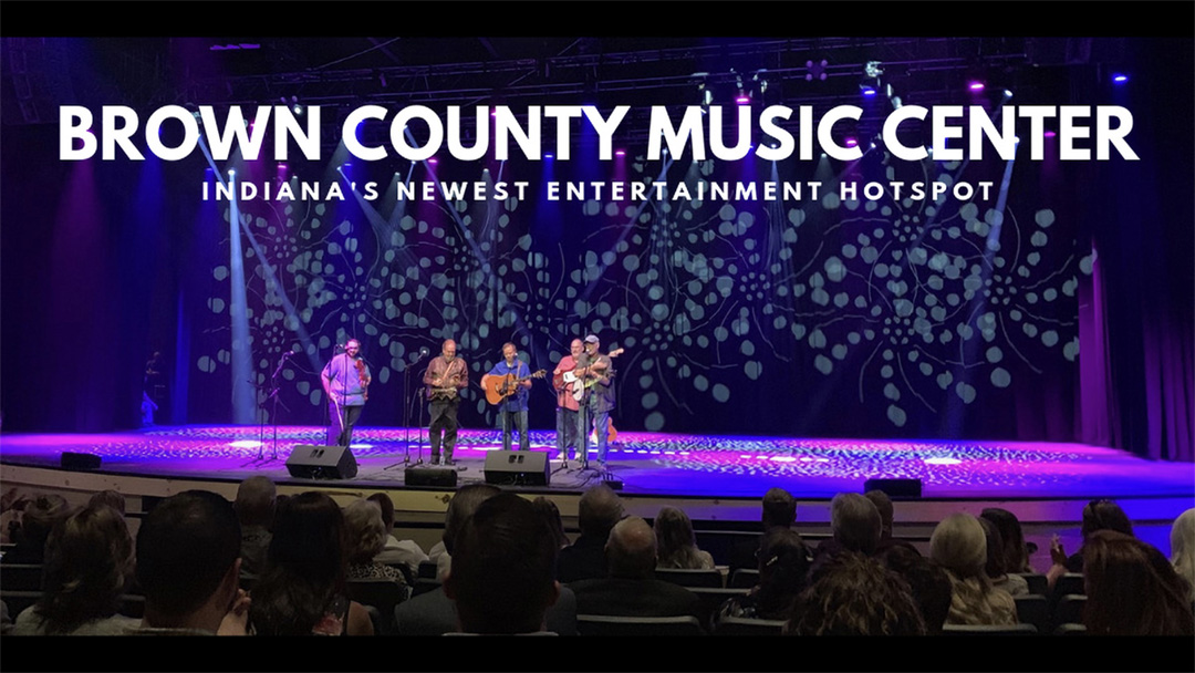 Wide shot of a band with 5 musicians on stage with purple and magenta lighting with text at the top of the image reading "Brown County Music Center, Indiana's Newest Entertainment Hotspot"