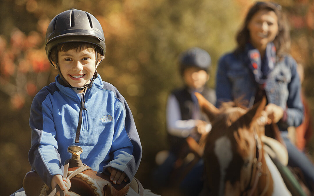 Smiling boy rides a horse with his mom and sibling