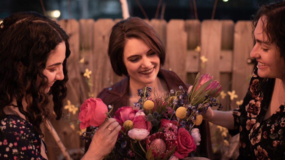 Three young women from the bridal party look over a floral bouquet