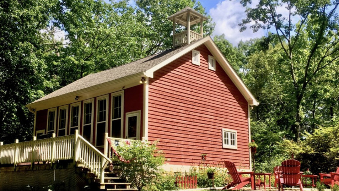 Exterior low angle image of red Schoolhouse Inn with bright red Adirondack chairs on a patio in the foreground