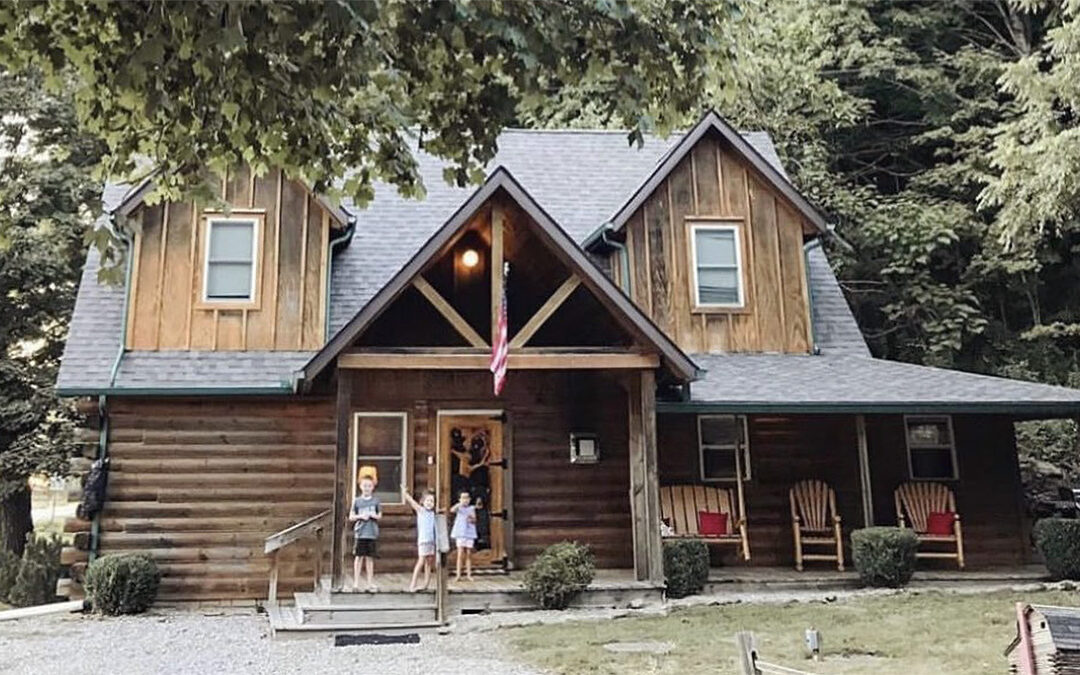 Three young children standing on the porch of a cozy cabin