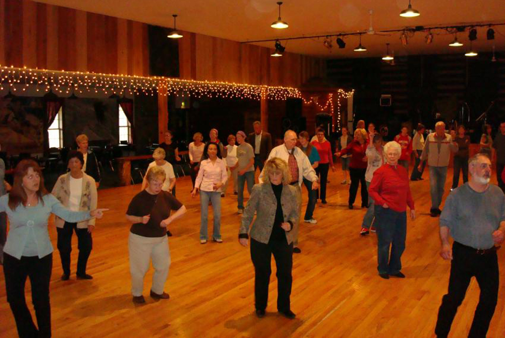 Evening exterior of an old barn wiht lights hanging over a wood-plank dance floor